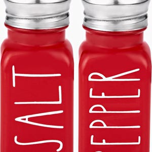 Puede incluir: Salero y pimentero de vidrio rojo con letras blancas. El salero dice "SALT" y el pimentero dice "PEPPER".