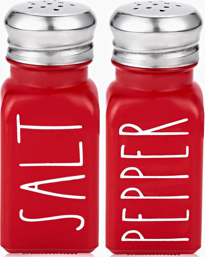 Puede incluir: Salero y pimentero de vidrio rojo con letras blancas. El salero dice "SALT" y el pimentero dice "PEPPER".