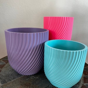 May include: Three decorative plant pots in different sizes. The largest pot is purple, the middle pot is pink, and the smallest pot is light blue. All three pots have a spiral design.