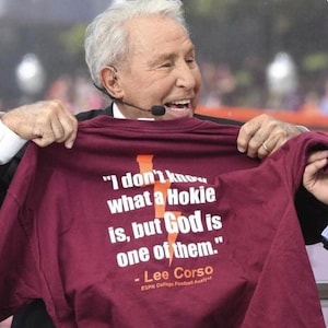 May include: A maroon t-shirt featuring white text that reads, "I don't know what a Hokie is, but God is one of them." The design includes an orange lightning bolt graphic behind the text and the name "Lee Corso" with "ESPN College Football Analyst."