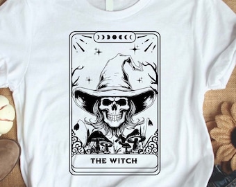 May include: White t-shirt with a black and white illustration of a tarot card featuring a skeleton wearing a witch's hat and holding a staff. The card reads "The Witch".