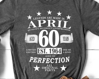 Peut inclure: T-shirt gris foncé avec texte blanc : "LEGENDS ARE MADE IN APRIL" et "AGED 60 YEARS". Le t-shirt affiche également "EST. 1964" et "AGED TO PERFECTION". L'image comprend un pantalon beige, un sac en cuir et des chaussures noires.