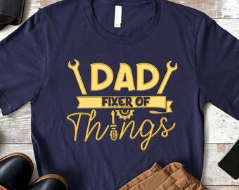 May include: A navy blue t-shirt with the text "DAD FIXER OF THINGS" in yellow with wrench graphics.