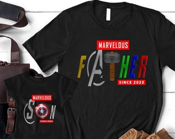 May include: Black t-shirts with a Marvel theme. The father's shirt says "Marvelous Father Since 2023" with the Avengers logo and Thor's hammer. The son's shirt says "Marvelous Son Since 2023" with Captain America's shield.