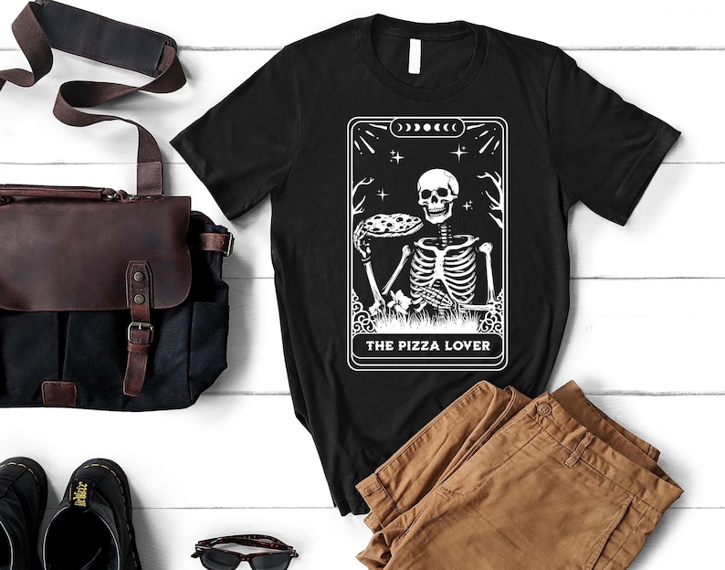 May include: Black t-shirt with a white graphic of a skeleton holding a pizza slice. The graphic is in the style of a tarot card and reads "The Pizza Lover".