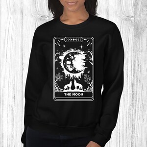 May include: Black sweatshirt with a white graphic of a tarot card, "The Moon", featuring a crescent moon, two wolves, and stars.