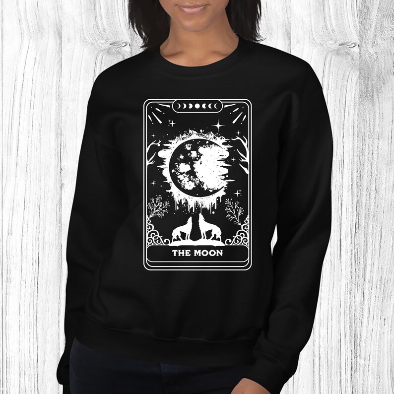 May include: Black sweatshirt with a white graphic of a tarot card, "The Moon", featuring a crescent moon, two wolves, and stars.