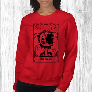 May include: Red sweatshirt with a black and white tarot card design featuring a full moon, two wolves, and the text "THE MOON".