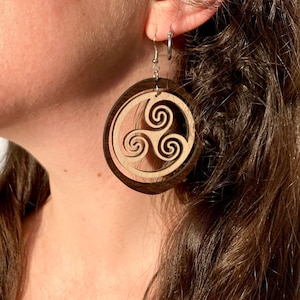 May include: A pair of wooden earrings with a brown and light brown wood design. The earrings feature a Celtic knot design with three spirals.