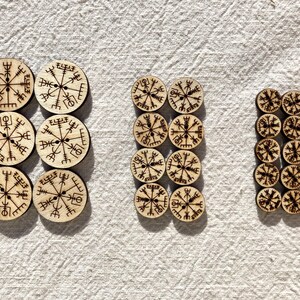 Può includere: Una collezione di bottoni in legno con un design a bussola e rune. I bottoni sono disposti in tre gruppi, con il gruppo più grande al centro.