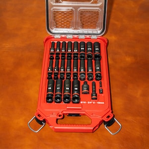 Könnte beinhalten: Eine rote Werkzeugkiste mit transparentem Deckel, geöffnet, um einen Satz schwarzer Steckschlüssel und Bits freizugeben. Die Steckschlüssel sind mit Größen von 8 bis 19 mm beschriftet. Die Werkzeugkiste hat einen Griff und Metallverschlüsse.