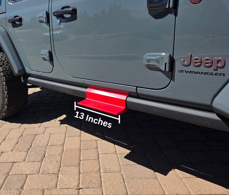 May include: A bright red metal step accessory attached to the side of a gray Jeep Wrangler vehicle. The step features a flat horizontal surface and a vertical support, with a white graphic label indicating a length of 13 inches.