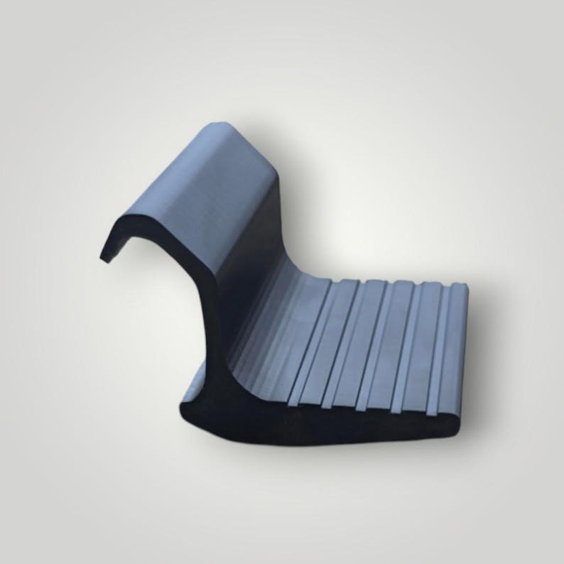May include: A dark gray, L-shaped rubber component featuring a curved top hook section and a flat, rectangular base with a series of parallel, raised ridges running across the surface to provide a textured, non-slip grip for industrial use.