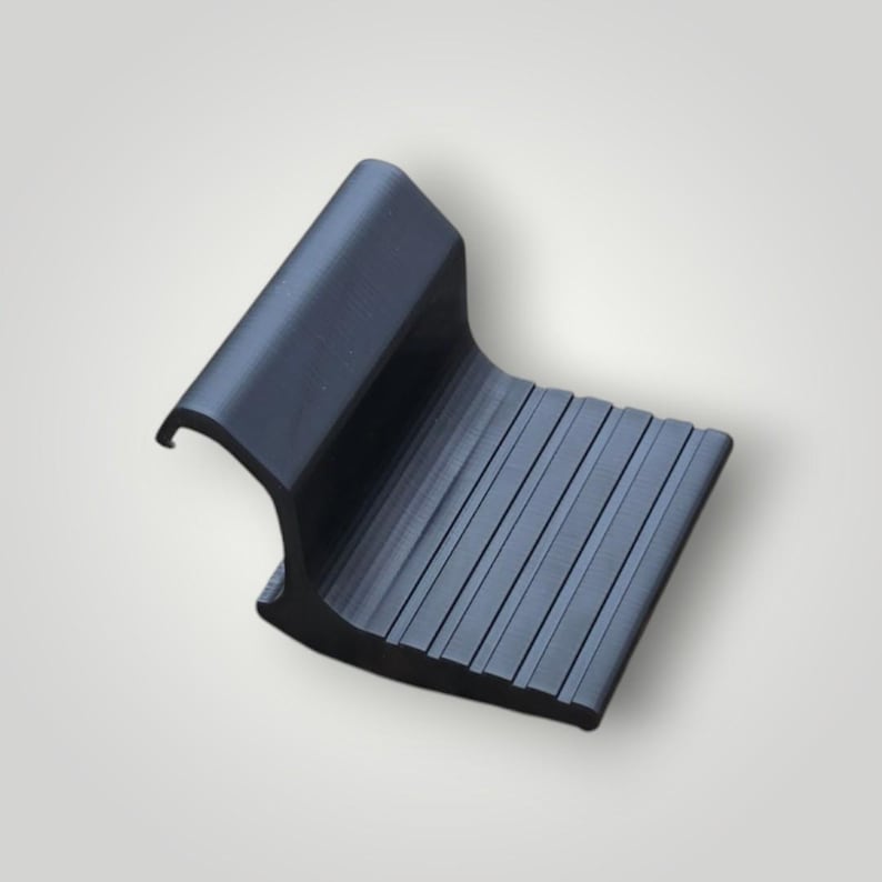 May include: A matte black plastic component featuring a curved hook-shaped top section and a flat, rectangular base with a series of parallel, raised ridges running across the surface, designed for secure placement or attachment.