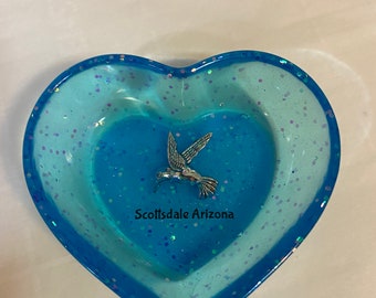 May include: A blue heart-shaped dish with a silver hummingbird charm and the text "Scottsdale Arizona" in white.