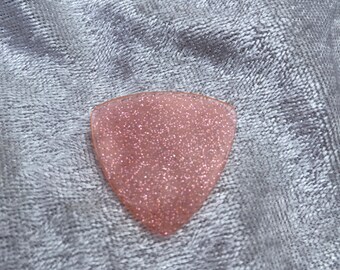 May include: A pink guitar pick with a sparkly finish.