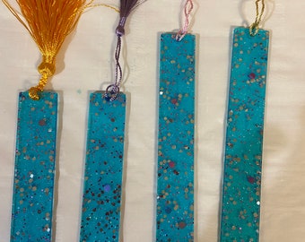 May include: Four turquoise blue bookmarks with silver glitter and a white inscription that reads "Scottsdale Arizona". Each bookmark has a different colored tassel attached: yellow, purple, pink, and gold.