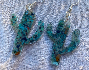 May include: A pair of silver cactus earrings with a green, blue, and brown speckled design.