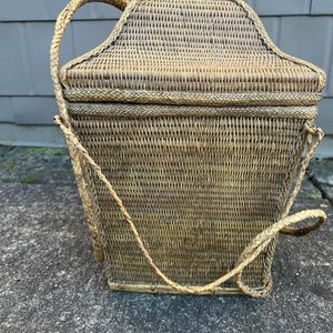 May include: A woven wicker basket with a lid and a long handle. The basket is made of natural materials and has a rustic look.