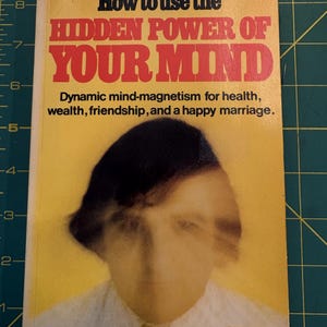 Peut inclure: Un livre de poche intitulé How to use the HIDDEN POWER OF YOUR MIND avec une couverture jaune présentant le portrait flou d'une personne en chemise blanche et cravate. Le texte inclut le sous-titre Dynamic mind-magnetism for health, wealth, friendship, and a happy marriage, le logo Coles et une règle visible mesurant environ 21,5 cm de hauteur.