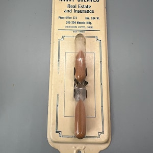 May include: White metal egg timer with a glass tube filled with brown sand. The timer is attached to a sign that reads "HARRY GREAVES Real Estate and Insurance Phone Office 273 Res. 634 W. 203-204 Masonic Bldg. OREGON CITY, ORE. EGG TIMER"