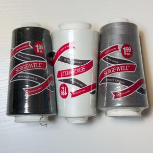 May include: Three large spools of Serge-Well serger thread in black, white, and gray. Each spool is labeled 100% polyester, 3000 yards (2742m), and made in China. The cylindrical spools feature a red and white banner design with brand text.