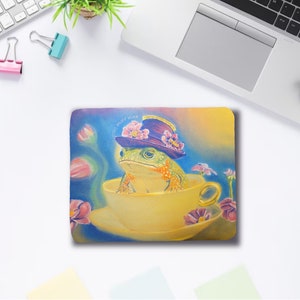 May include: A green frog wearing a purple hat with pink flowers sits in a yellow teacup with a saucer. The frog is surrounded by pink and purple flowers on a blue background.