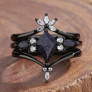 Könnte beinhalten: Schwarzer Ring mit einem blauen sternförmigen Stein und weißen Diamanten. Der Ring hat ein zartes, florales Design.