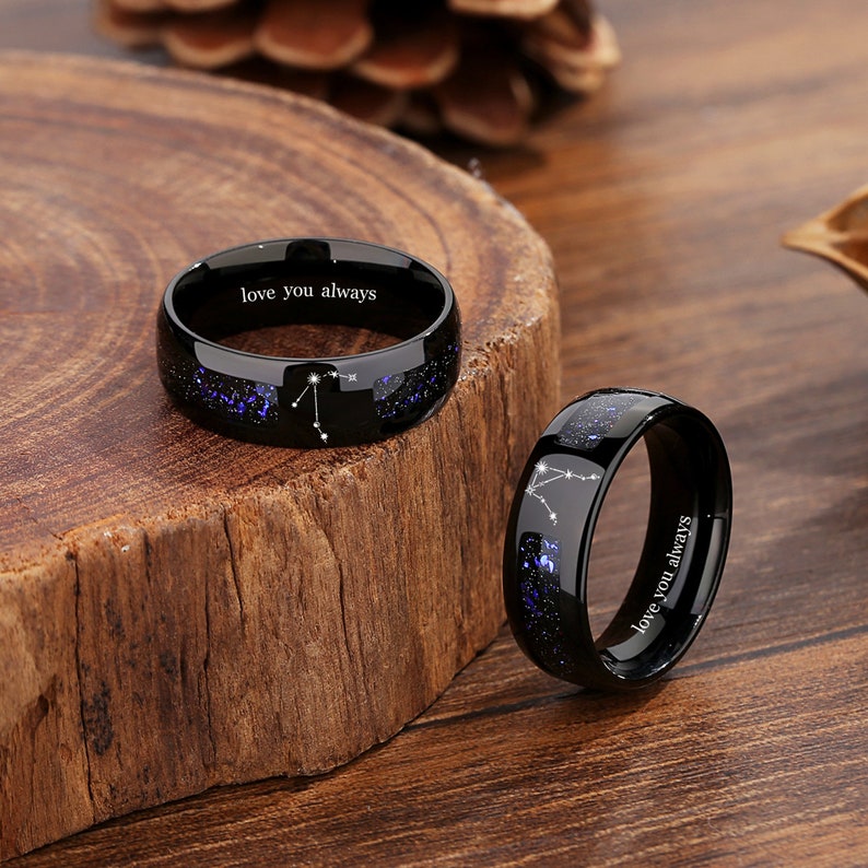 May include: Two black tungsten carbide rings with a constellation design and the inscription "love you always".
