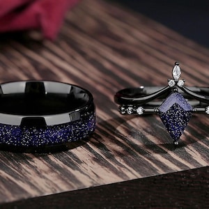 May include: A pair of wedding bands, one with a black finish and blue glitter, and the other with a black finish and a blue gemstone.