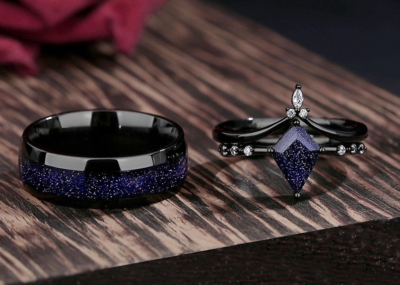 May include: A pair of wedding bands, one with a black finish and blue glitter, and the other with a black finish and a blue gemstone.