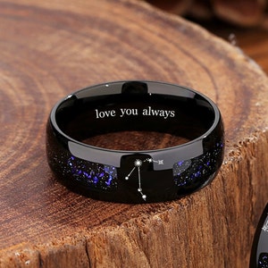 May include: Black tungsten carbide ring with a constellation design and the inscription "love you always".