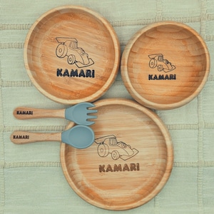 May include: A set of three wooden plates and two utensils. Each plate features a black race car graphic and the name "KAMARI". The utensils have wooden handles and gray silicone heads. The plates are approximately 6 inches in diameter.