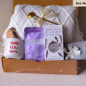 May include: A gift box filled with self-care items, including a white mug with the text "mama MAMA nama" in red, a purple package labeled "COLLAGEN IRMING", a white bath salt package with lavender scent, and a gray knitted sock.