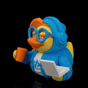 Op de afbeelding: Een geel rubberen eendje met een blauwe hoodie, blauwe koptelefoon en blauwe bril. De eend heeft oranje haar en een oranje snavel, houdt een oranje beker in de ene vleugel en een witte laptop in de andere. Een wit shirt met een code-symbool.