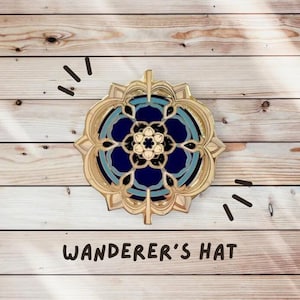 Può includere: Spilla in smalto dorato e blu con un design a mandala. La spilla presenta un motivo circolare con un fiore centrale e dettagli intricati. Il testo "WANDERER'S HAT" è sotto la spilla.