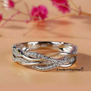 May include: A silver band ring with a delicate, intertwined design. The band is accented with small, clear gemstones.