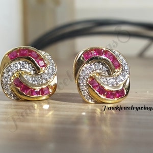 May include: A pair of gold earrings with a knot design. The earrings are set with small red and white stones.