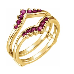 May include: A yellow gold ring guard featuring a chevron-shaped design adorned with ten round-cut, deep pinkish-red rubies. The band has a polished finish and is structured to frame another ring, showcasing a V-shaped contour set with gemstones.