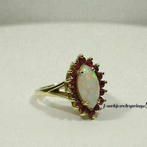 May include: A gold ring featuring a white opal gemstone set in a halo of red rubies.