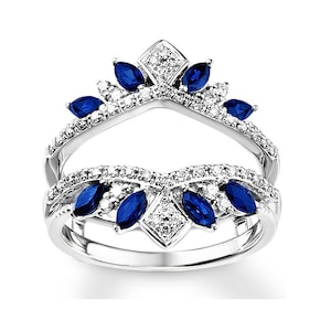 May include: A silver ring with a split shank design. The ring is set with marquise-shaped blue sapphires and round brilliant diamonds. The ring is designed to be worn with a separate engagement ring.