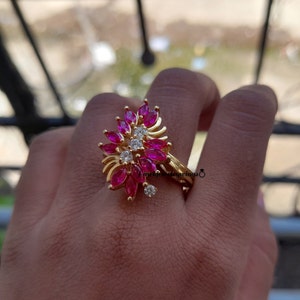 May include: A gold ring with a pink and white flower design. The ring is set with small pink and white stones.