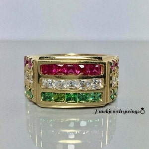 May include: A gold band ring with red, white, and green gemstones. The ring has a square shape and is set with multiple rows of gemstones.
