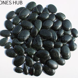 May include: A large group of dark green, oval-shaped stones with a glittery finish. The stones are arranged in a circular pattern on a white background.