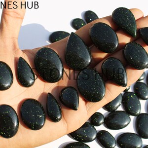 May include: A collection of green aventurine gemstone cabochons in various shapes and sizes. The cabochons have a sparkly, glittery finish.
