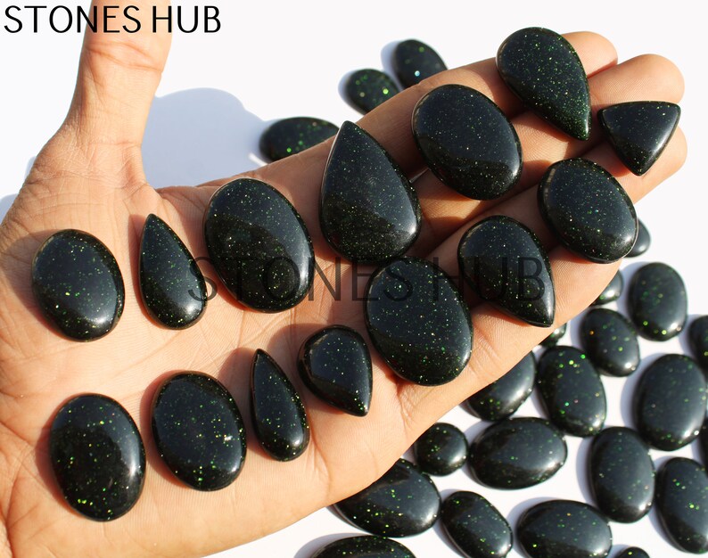 May include: A collection of green aventurine gemstone cabochons in various shapes and sizes. The cabochons have a sparkly, glittery finish.