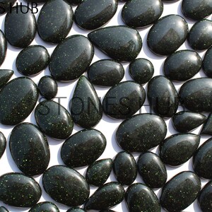 May include: A collection of green and black gemstone cabochons with a sparkly finish. The stones are various shapes and sizes, including oval, teardrop, and round.
