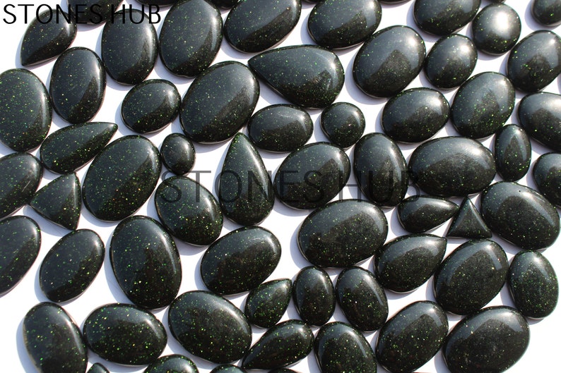 May include: A collection of green and black gemstone cabochons with a sparkly finish. The stones are various shapes and sizes, including oval, teardrop, and round.