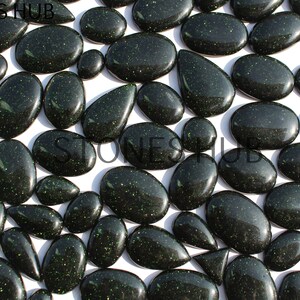 May include: A collection of green aventurine cabochons with a sparkly, glittery finish. The cabochons are various shapes and sizes, including oval, pear, and teardrop.