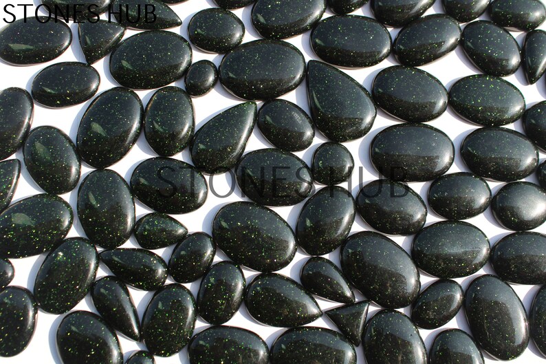 May include: A collection of green aventurine cabochons with a sparkly, glittery finish. The cabochons are various shapes and sizes, including oval, pear, and teardrop.